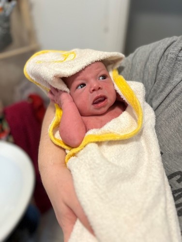 A baby being held whilst wrapped in a drying towel looking up.