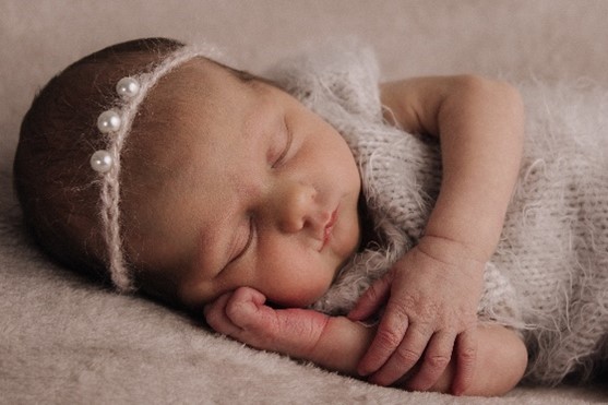 A baby lying on its side, hand of its face asleep.
