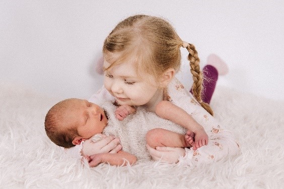 A small child lying down, cuddling a baby whilst looking at her.