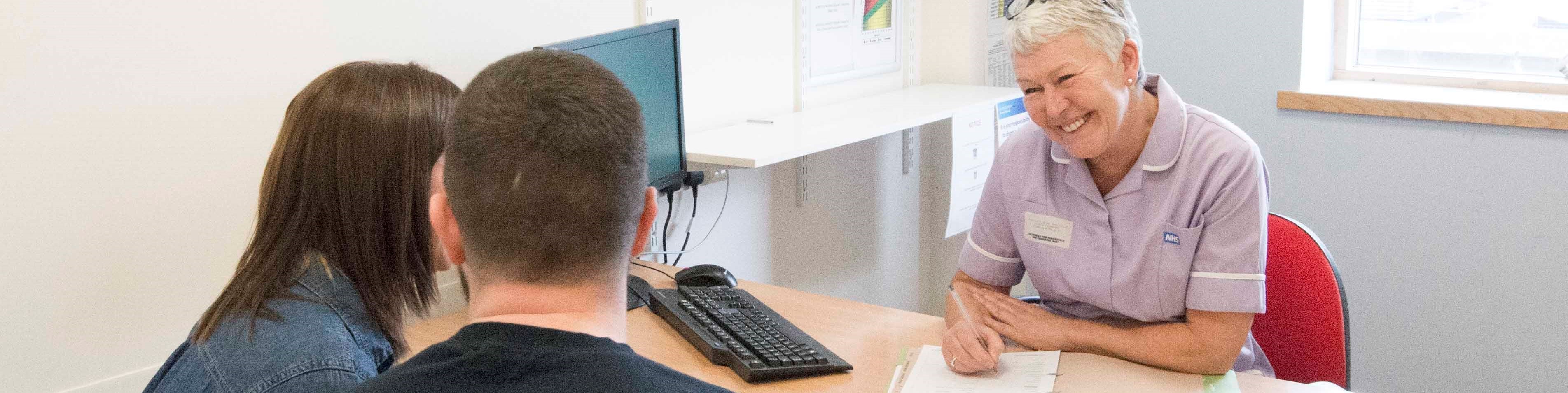 A couple and a nurse sitting at a computer desk.