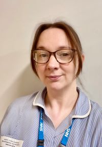 A person wearing glasses has short brunette hair and is dressed in a blue and white uniform.