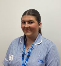 A person is smiling with tied-back brunette hair and is dressed in a blue and white uniform.