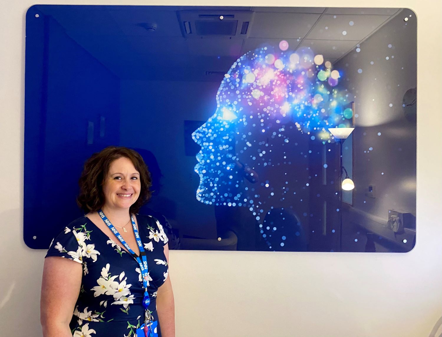 A person smiling while standing in front of a picture of a brightly coloured silhouette human head.