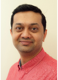 A person with short black hair, smiling in a pink shirt.