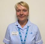 A person smiling with short blonde hair, and a blue uniform and blue lanyard.