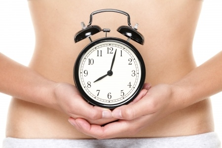 A woman holding an old clock in both palms in front of her stomach.